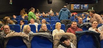 Uczestnicy siedzący na niebieskich fotelach w sali kinowej